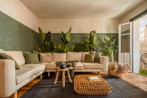salón decorado en verde con plantas de interior y sofá rinconera beige
