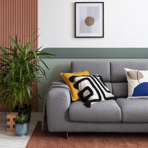 salón de diseño moderno con sofá gris, pared pintada con formas geométricas y moldura decorativa en color teja