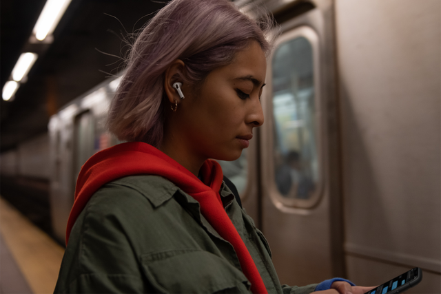 young girl wearing airpods pro looking at her iphone in subway station