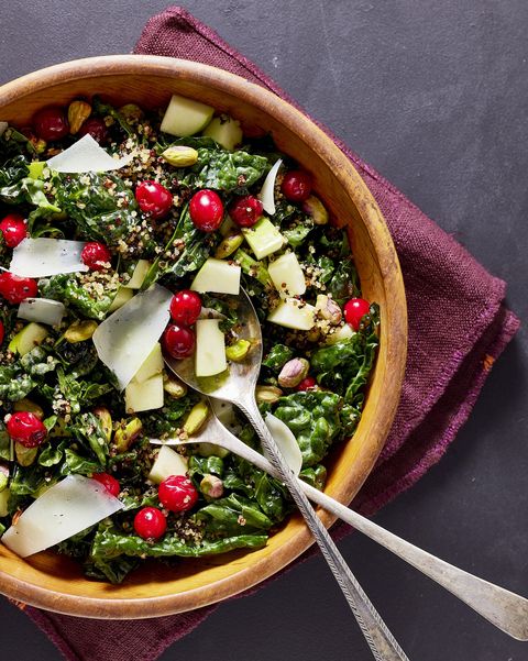 kale salad with pickled cranberries and crispy quinoa in a wooden serving bowl topped with apple chunks and shaved manchego