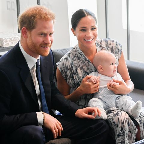 Prince Harry, Meghan Markle and their young son, Archie, during a trip of Africa. Archie is sat on Meghan's lap and the parents are both smiling.