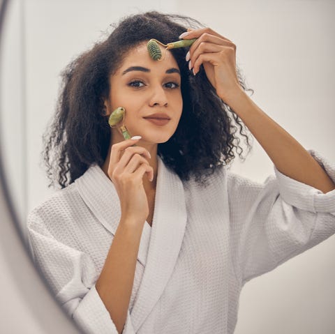 portrait of a woman massaging her face with jade rollers in front of the mirror