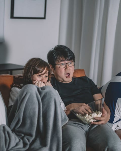 asian chinese couple watching scary horror tv show at night during weekend in living room sitting on sofa