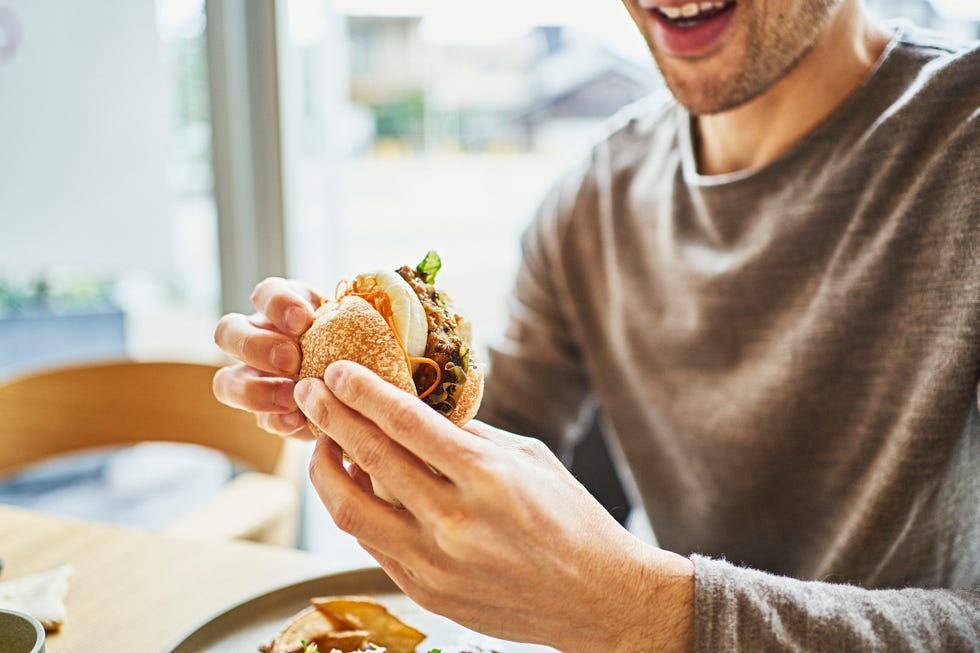 asian-man-eating-a-veggie-burger-at-a-vegan-cafe-royalty-free-image-1682674669.jpg?crop=1.00xw:1