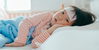 Asian sick little girl lying in bed with a high fever