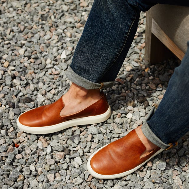 brown sneakers and blue jeans on model against gravel background