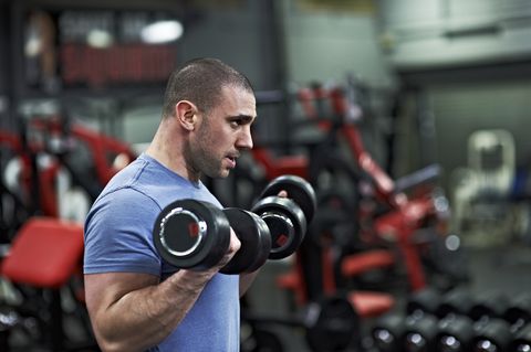 Athletic Male Lifting Dumbbells in Gym