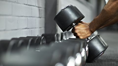 Athletic Male Picking Up Dumbbells in Gym