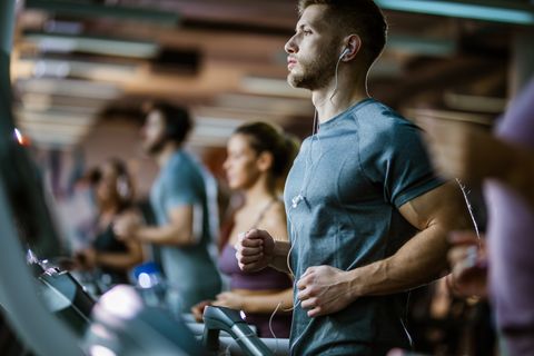 Athletic man listening music while running on treadmill in a gym.