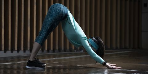 Athletic woman doing downward dog yoga pose on street at night.