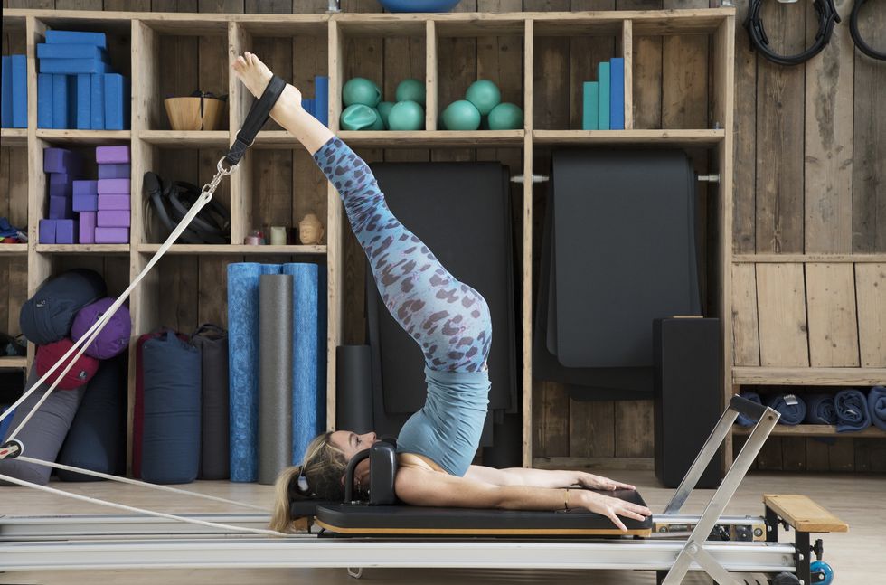 Athletic woman stretches on pilates reformer with legs in straps. 