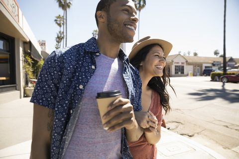 Smiling couple drinking coffee and walking on sunny sidewalk