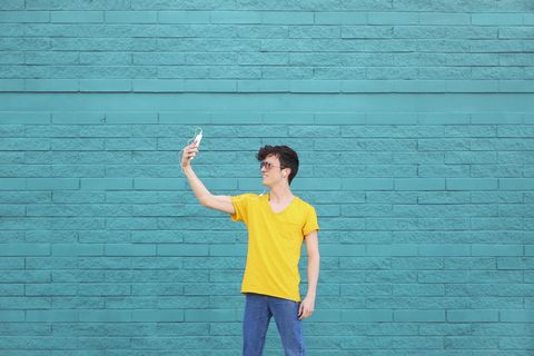 Young man taking a selfie with smartphone in front of blue brick wall