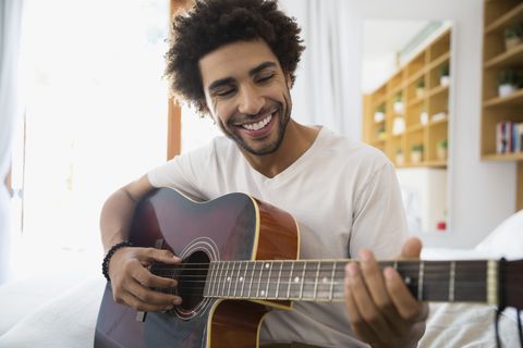 Smiling man playing guitar in bedroom