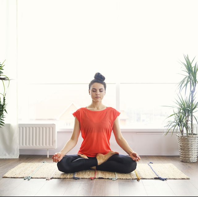 attractive young woman exercising and sitting in yoga lotus position while resting at home