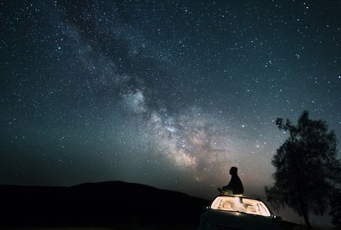 austria, mondsee, silhouette of man sitting on car roof under starry sky