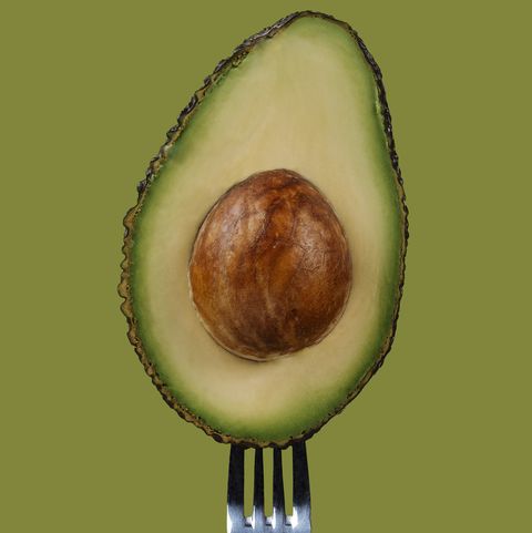 avocado in half on a fork on a light green background