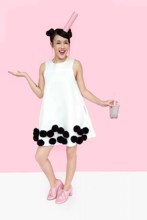 woman in white dress with black pom poms on bottom holding bubble tea with pink straw on head