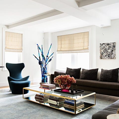 A List 2022 - ELLE DECOR living room area with brown sofa and two tier glass coffee table and teal colored armless chairs