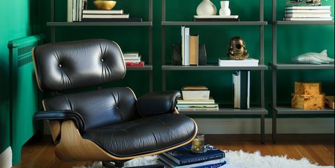 un estudio verde con un sillón eames y tres estantes con libros y otros objetos