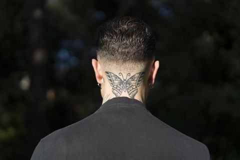vista traseira de um homem com uma borboleta tatuada no pescoço