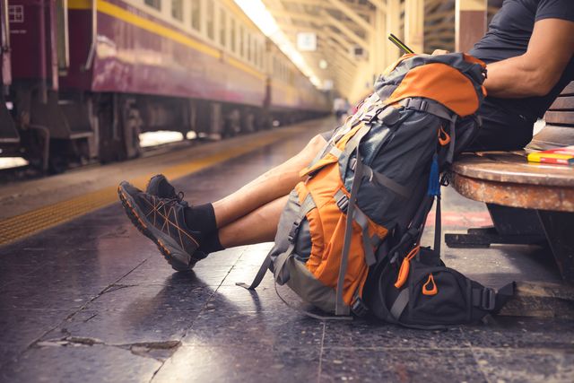 hombre con una mochila en una estación esperando el tren mientras consulta el móvil