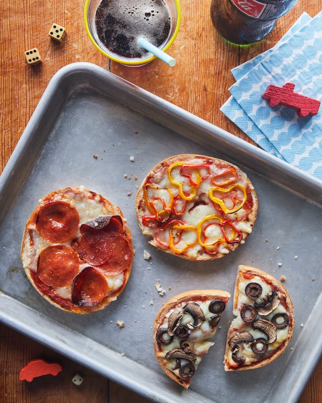 bagel pizzas on a tray with different toppings, toys and a drink near by