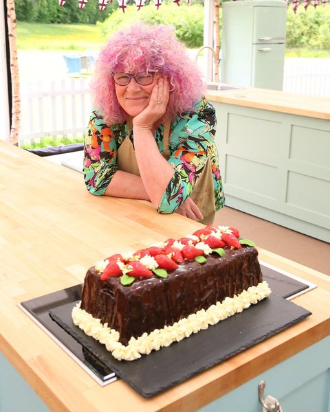 gran horneado británico, carole con la cabeza en la palma de la mano suspirando detrás de su pastel, decorado con fresas