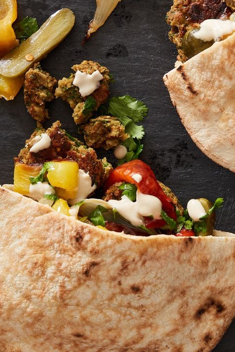 baked falafel with roasted peppers in a pita with tahini sauce on a black background