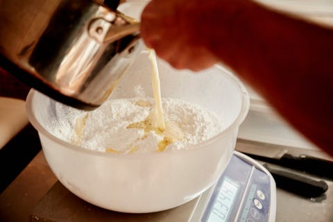 Un boulanger versant le liquide d'une cruche en cuivre dans un bol avec de la farine et des ingrédients pour la pâte. Un boulanger versant le liquide d'une cruche en cuivre dans un bol avec de la farine et des ingrédients pour la pâte.