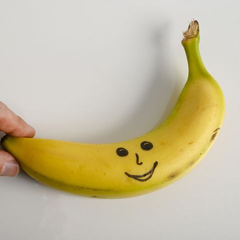 banana with a smiley face drawn a hand picks the banana conceptual nature