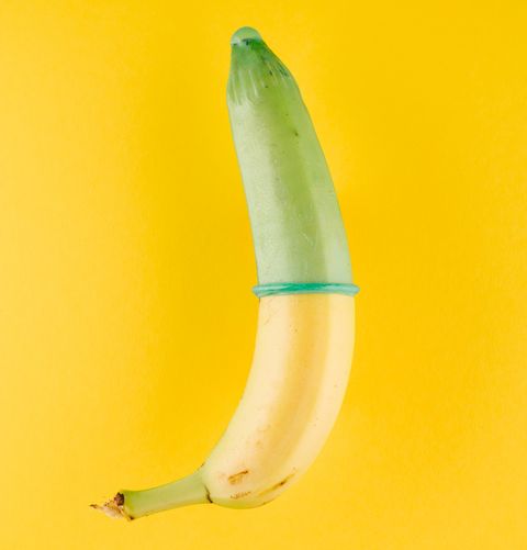 Banana with green condom in front of yellow background