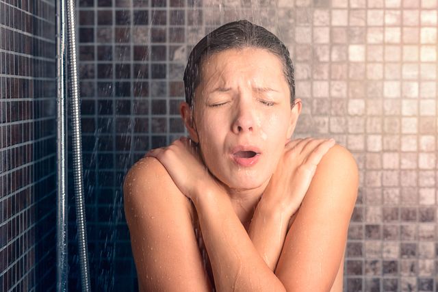 bare woman reacting while taking cold shower