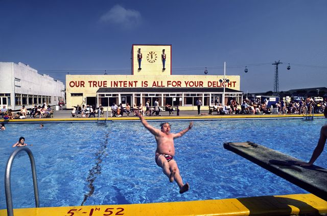 man falling backwards into swimming pool in butlins holiday camp, skegness the slogan 'our true intent is all for your delight' was borrowed from midsummers night's dream
