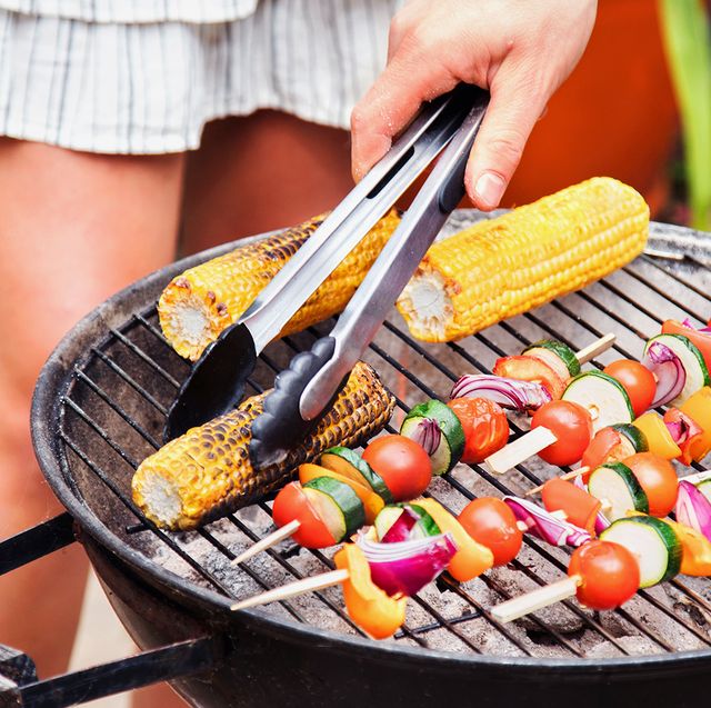 woman man and dog standing around charcoal bbq grill turning grilled corn and kebabs with tongs