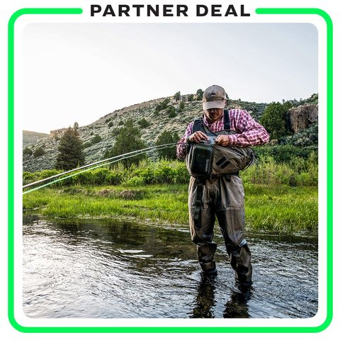 partner deal backcountry man looking in bag holding fishing rod while standing in lake