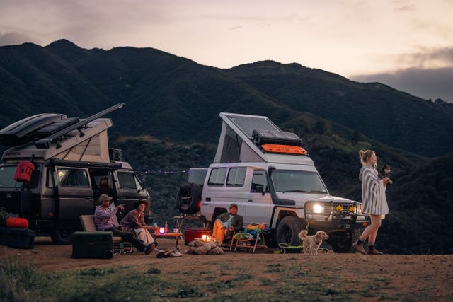 people sitting around a campfire next to their rv in the mountains with backcountry gear