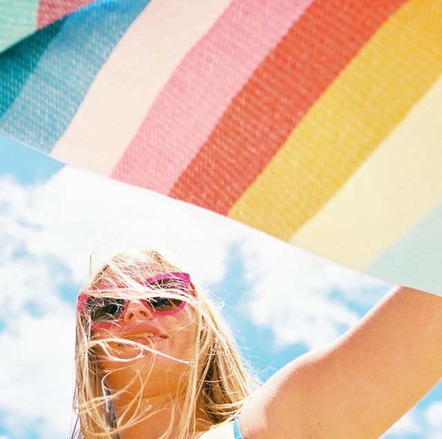 woman fanning striped beach blanket out against blue sky