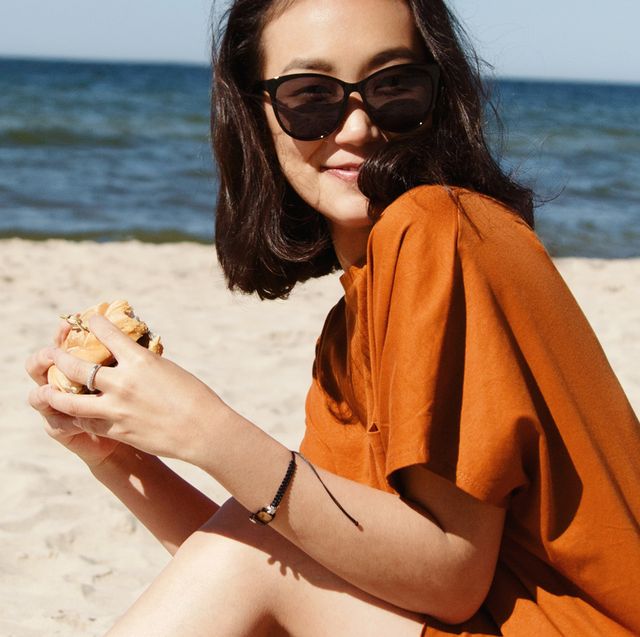 woman in sunglasses eating a burger on the beach