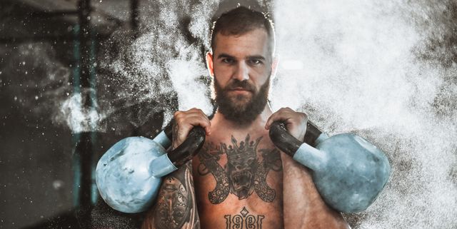 bearded male working out with kettlebells in gym