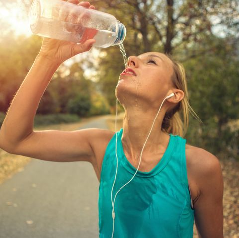 beautiful and sporty young woman drinking water after jogging outdoors