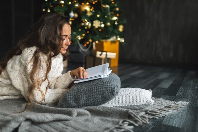 mujer leyendo libro junto a árbol de navidad