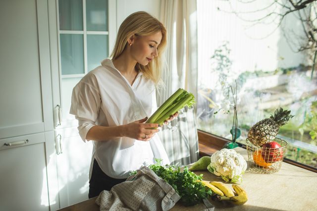 beautiful woman unpacks a full fabric bag with fruits and vegetables on the kitchen