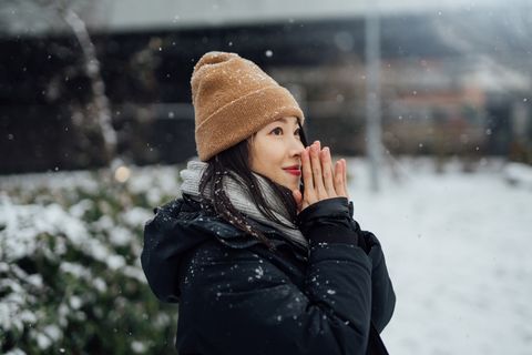 beautiful young asian woman warming her hands in the snow
