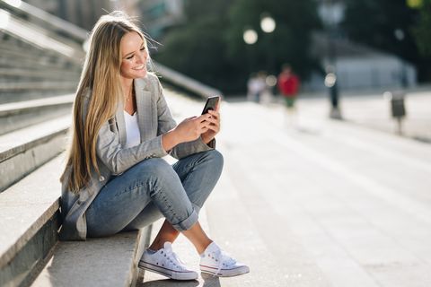 Beautiful young blonde woman looking at her smartphone and smiling.