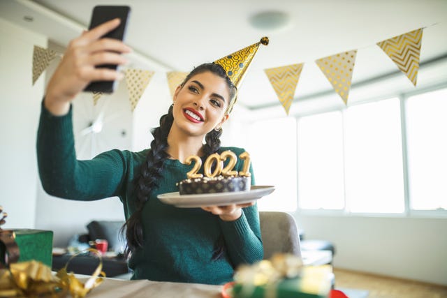 beautiful young woman having video call while she preparing for new year, making a cake and wrapping gifts