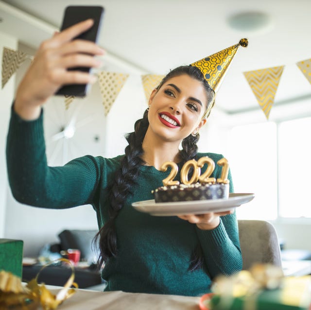 beautiful young woman having video call while she preparing for new year, making a cake and wrapping gifts