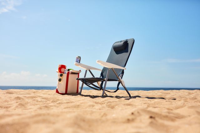 a beach chair and bag on sand next to the ocean