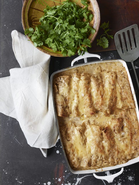 sour cream chicken enchiladas in a white rectangle baking dish with a bowl of fresh cilantro to the side