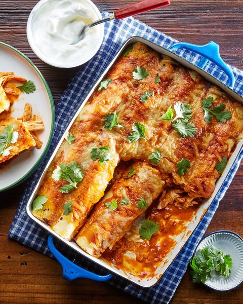 chicken enchiladas in red sauce in a blue baking dish on a blue checked cloth